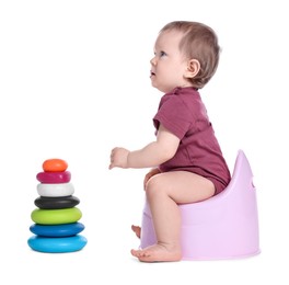 Photo of Little child with toy pyramid sitting on baby potty against white background