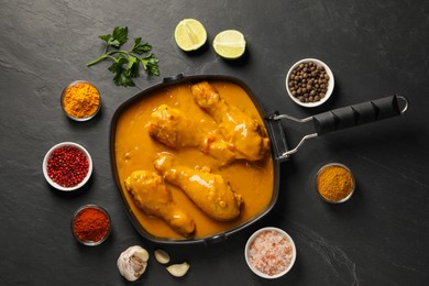 Photo of Tasty chicken curry and ingredients on black textured table, flat lay