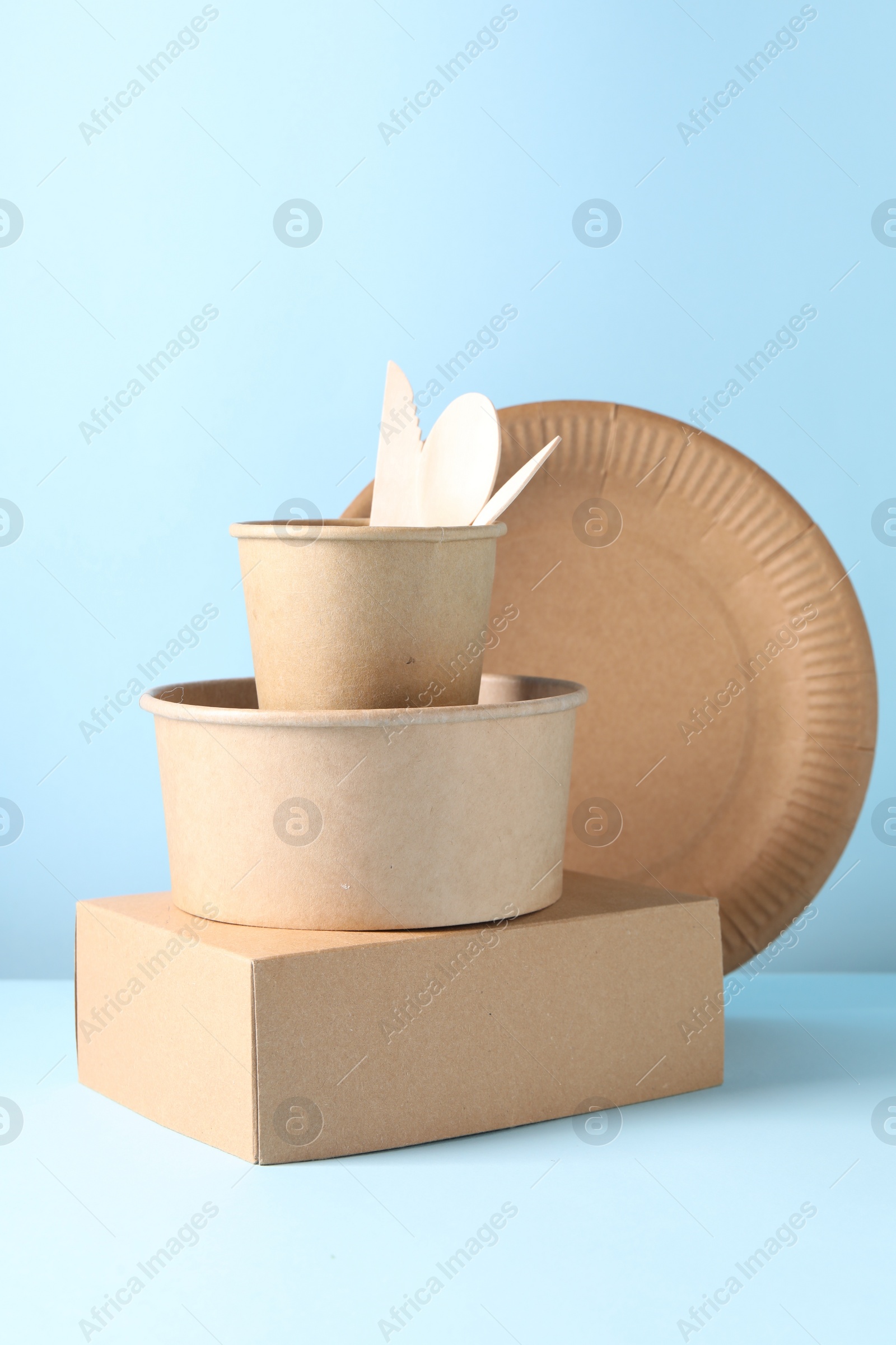 Photo of Eco friendly food packaging. Paper containers and tableware on white table against light blue background