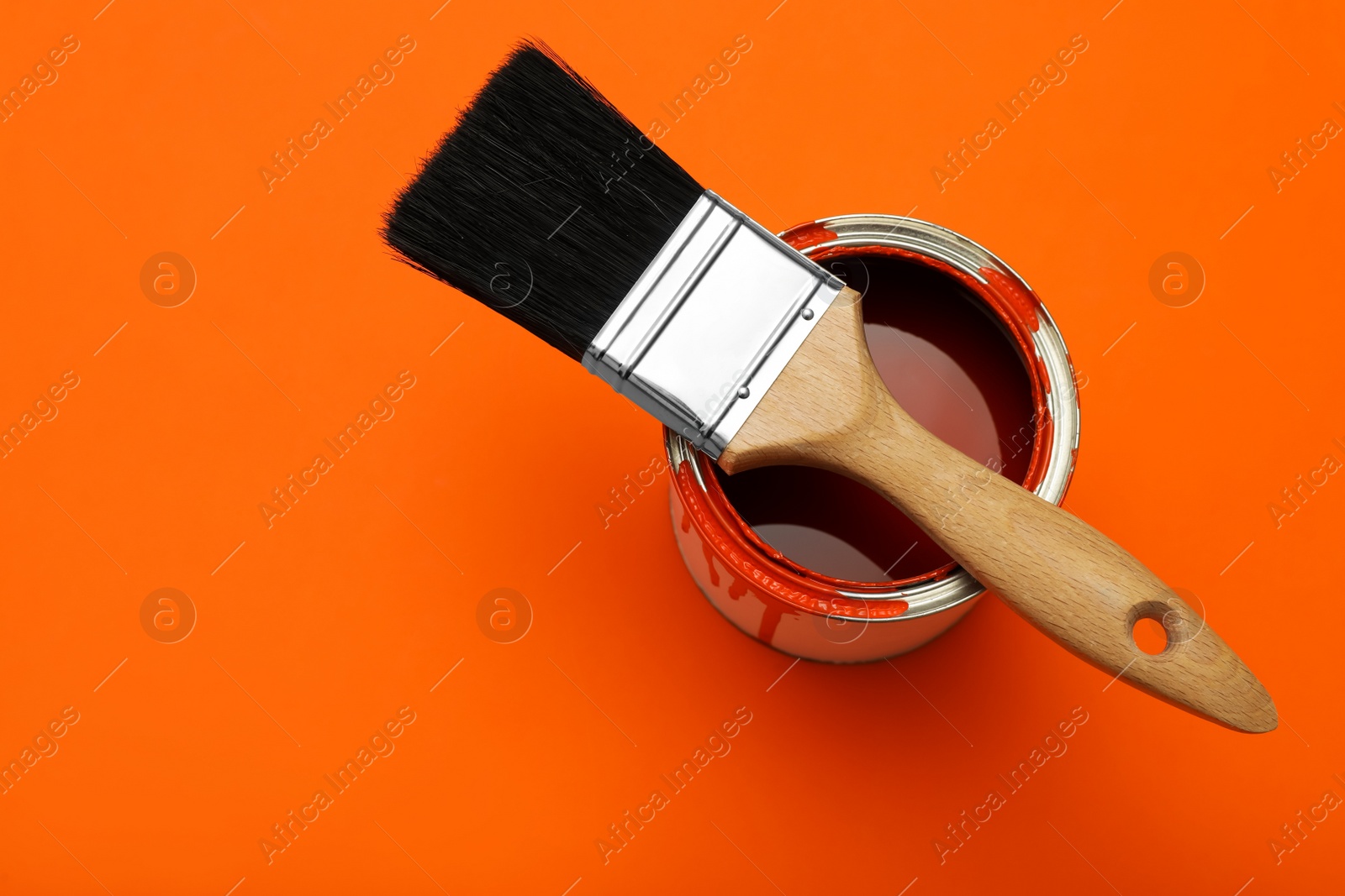 Photo of Can of orange paint and brush on color background, top view. Space for text