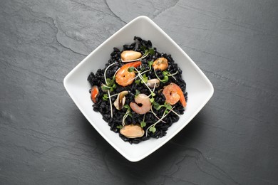 Photo of Delicious black risotto with seafood in bowl on grey table, top view