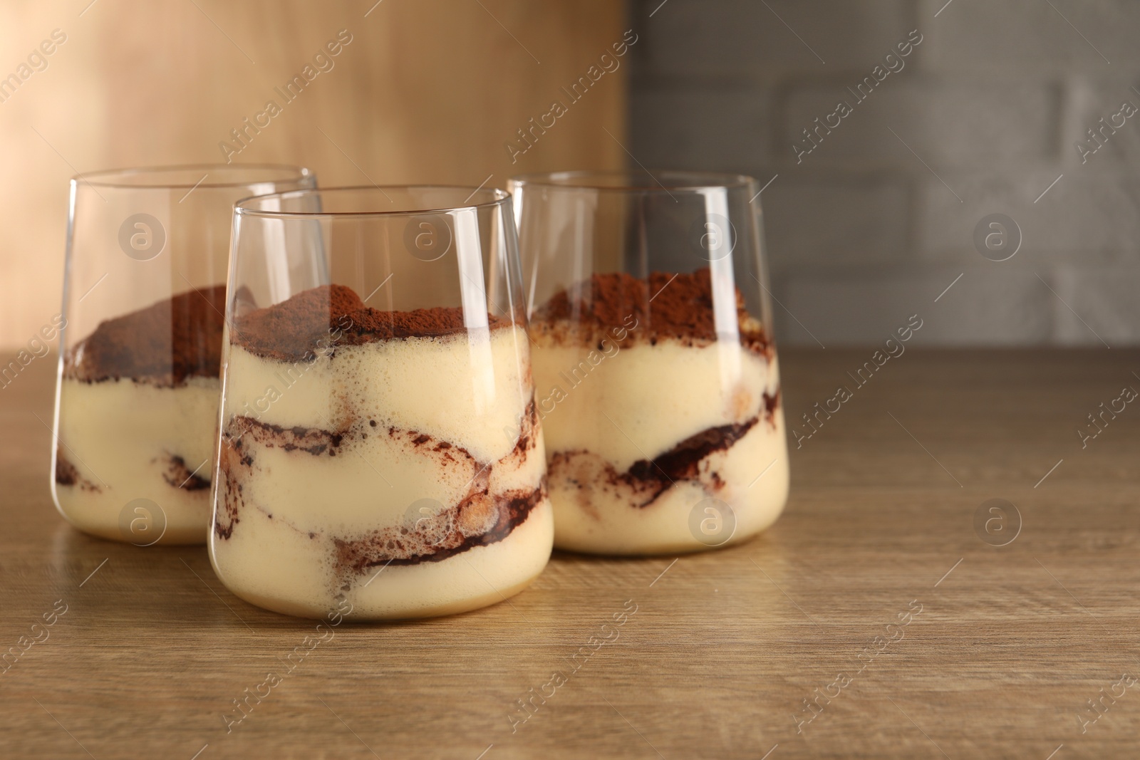 Photo of Delicious tiramisu in glasses on wooden table. Space for text