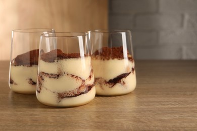 Photo of Delicious tiramisu in glasses on wooden table. Space for text