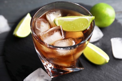 Glass of cocktail with cola, ice and cut lime on table