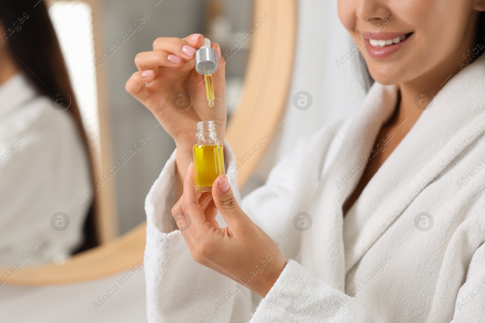 Photo of Young woman with serum in her hands in bathroom, closeup