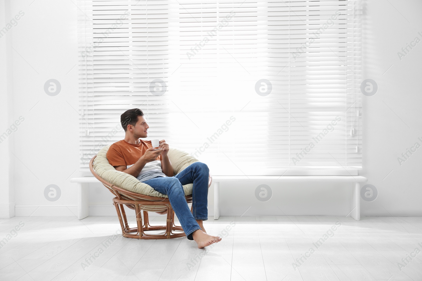 Photo of Attractive man relaxing in papasan chair near window at home. Space for text