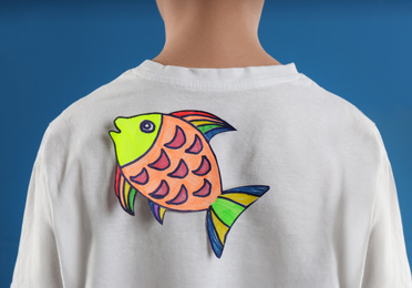 Photo of Preteen boy with paper fish on back against blue background,closeup. April fool's day