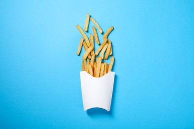 Photo of Paper cup with French fries on light blue table, flat lay