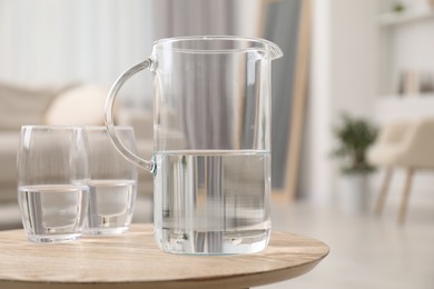 Photo of Jug and glasses with clear water on wooden table indoors, closeup. Space for text