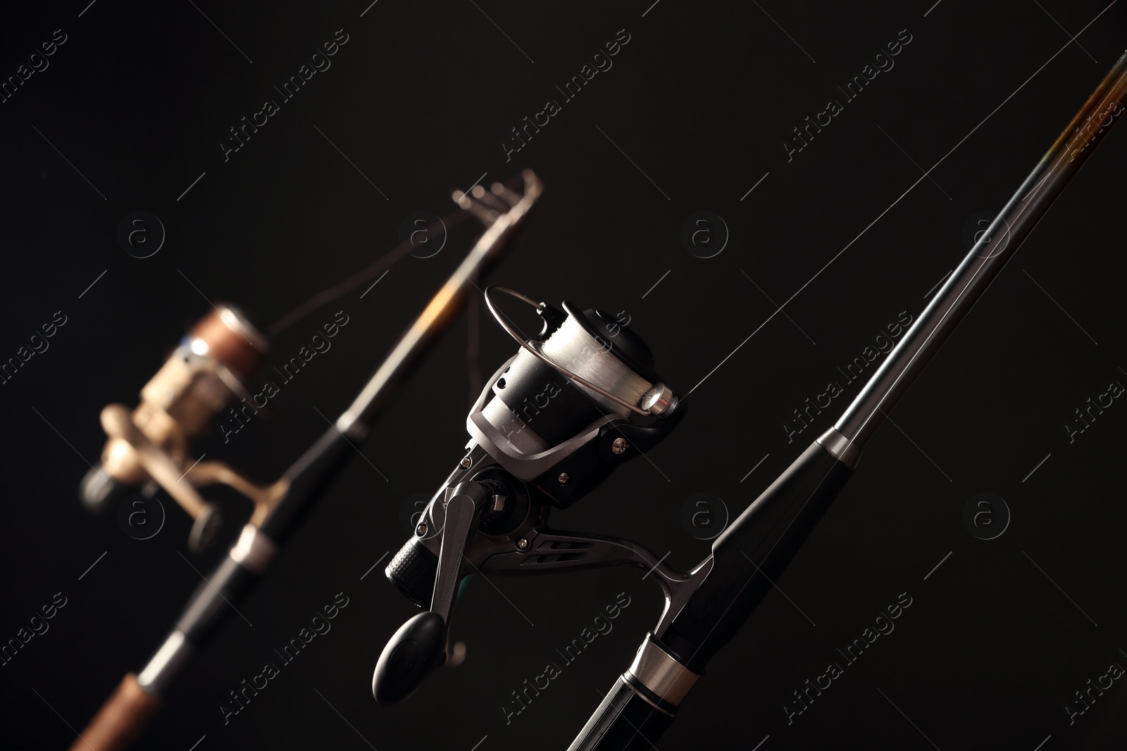 Photo of Modern spinning rod against dark background, closeup. Fishing equipment