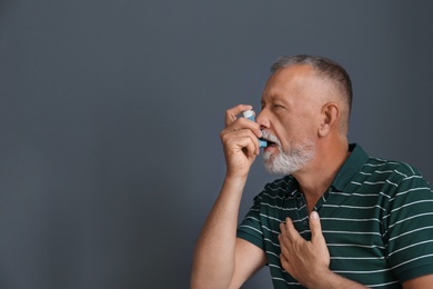 Man using asthma inhaler on color background with space for text