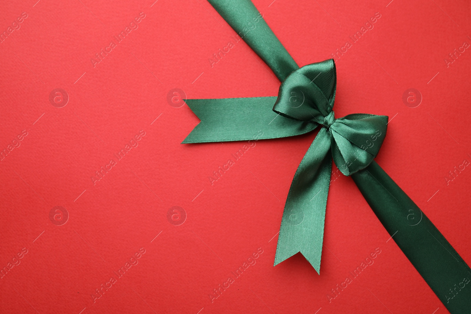 Photo of Green satin ribbon with bow on red background, top view. Space for text