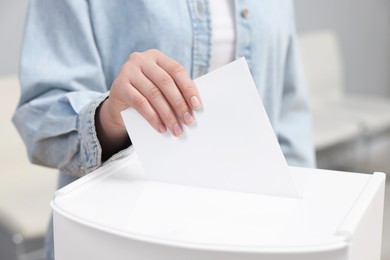 Photo of Woman putting her vote into ballot box on blurred background, closeup