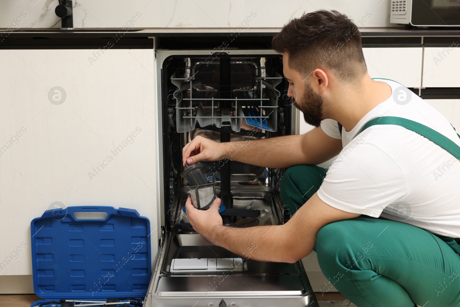 Photo of Repairman holding drain filter near dishwasher in kitchen