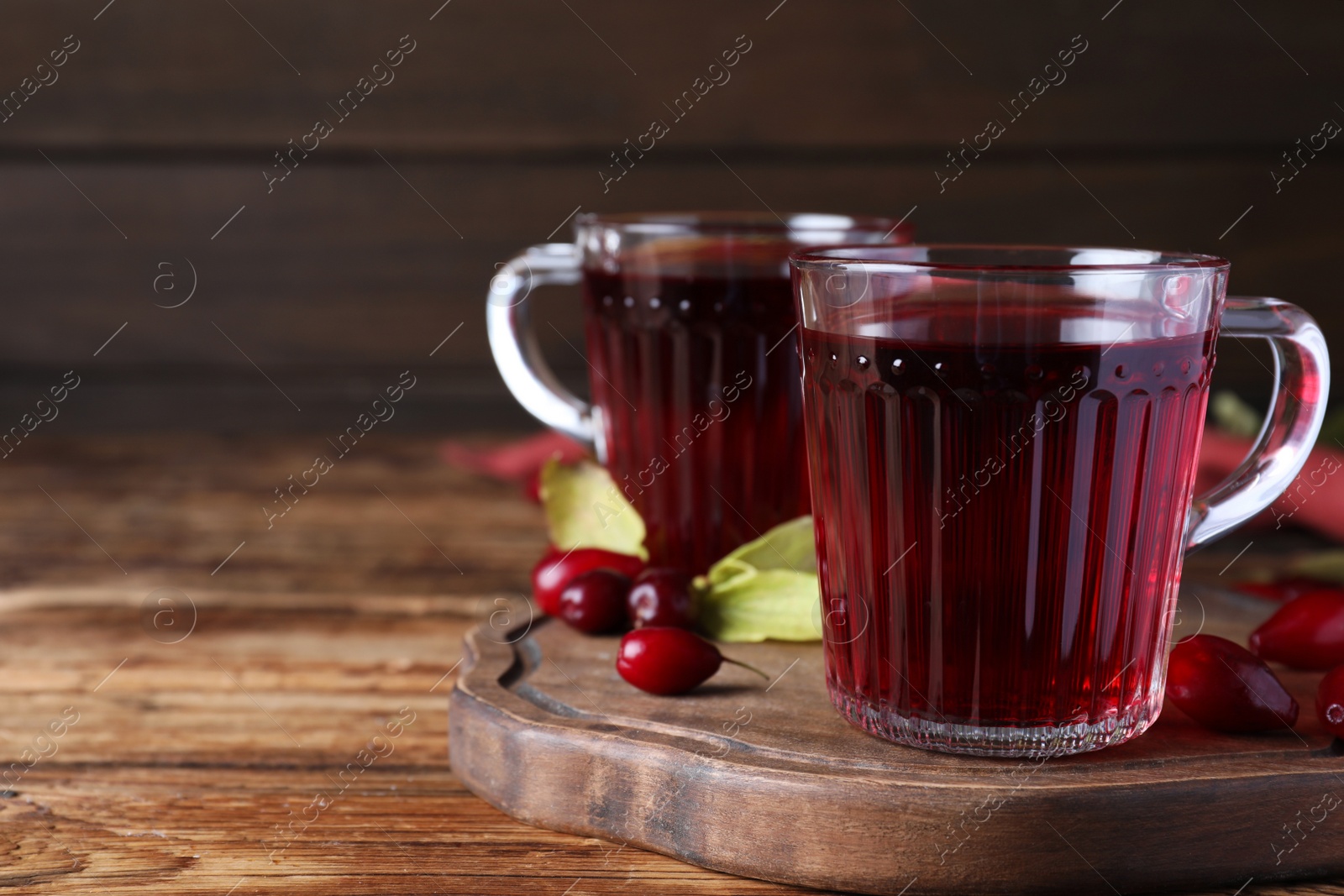 Photo of Glass cups of fresh dogwood tea and berries on wooden table. Space for text