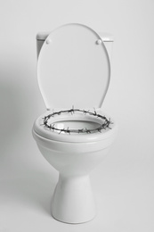 Toilet bowl with barbed wire on white background. Hemorrhoids concept