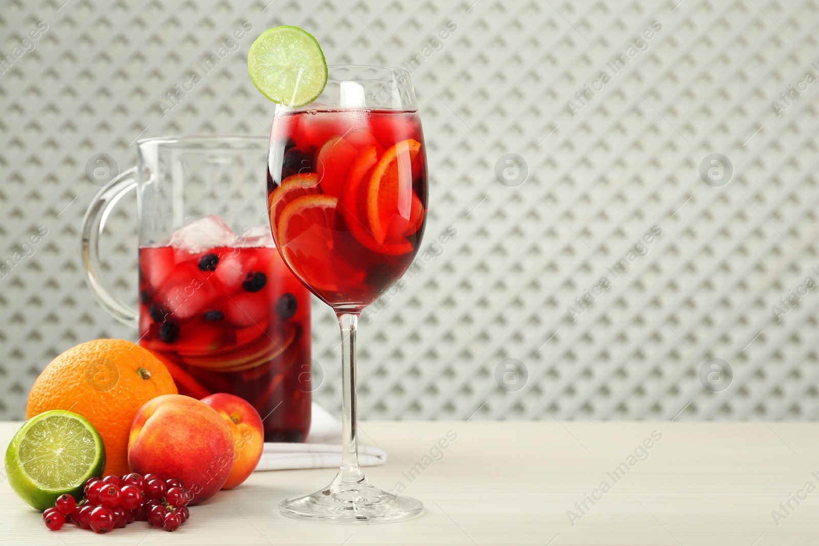 Photo of Glass and jug of Red Sangria with fruits on white wooden table, space for text