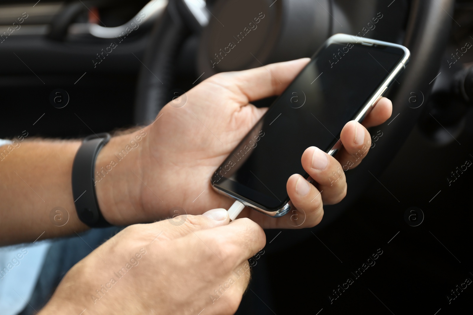 Photo of Man connecting charging cable to smartphone in car, closeup