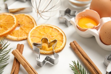 Photo of Cookie cutters, dried orange slices, cinnamon sticks and eggs on white table. Christmas biscuits