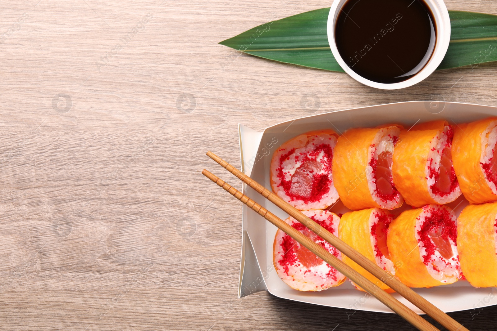 Photo of Food delivery. Delicious sushi rolls, chopsticks and soy sauce on wooden table, flat lay. Space for text