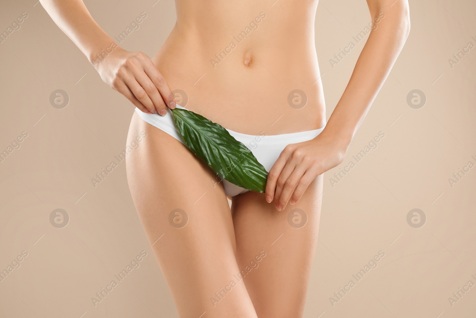 Photo of Woman with leaf showing smooth skin after bikini epilation on beige background, closeup. Body care concept