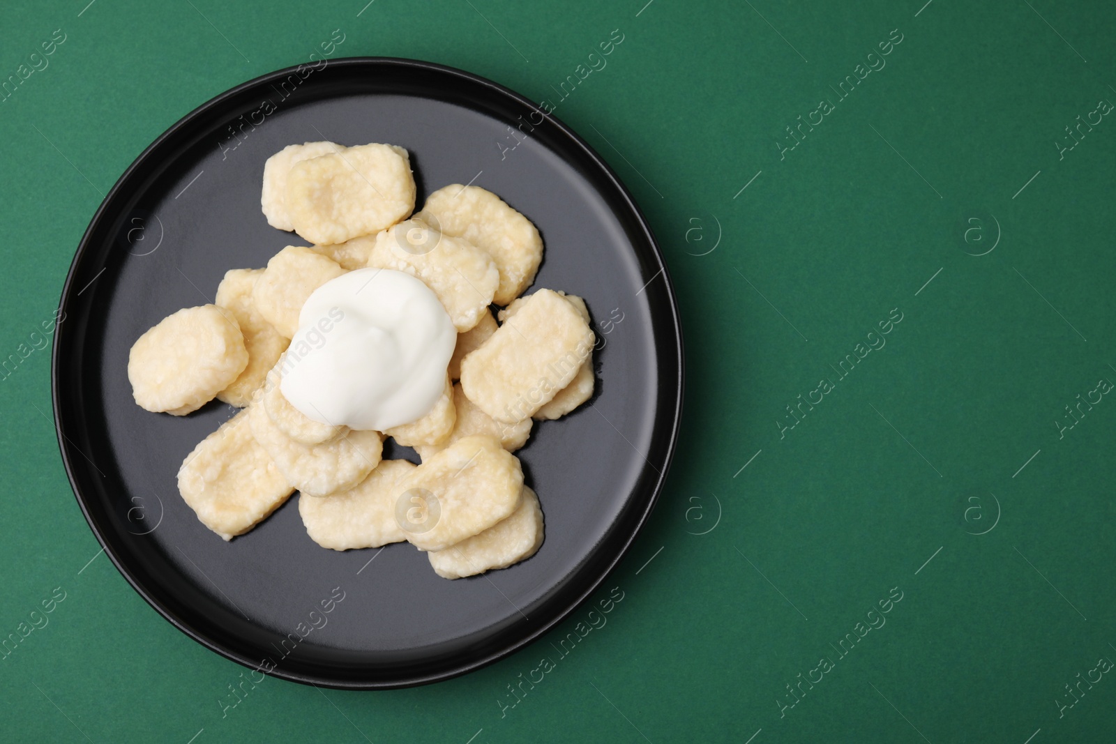 Photo of Plate of tasty lazy dumplings with sour cream on dark green background, top view. Space for text