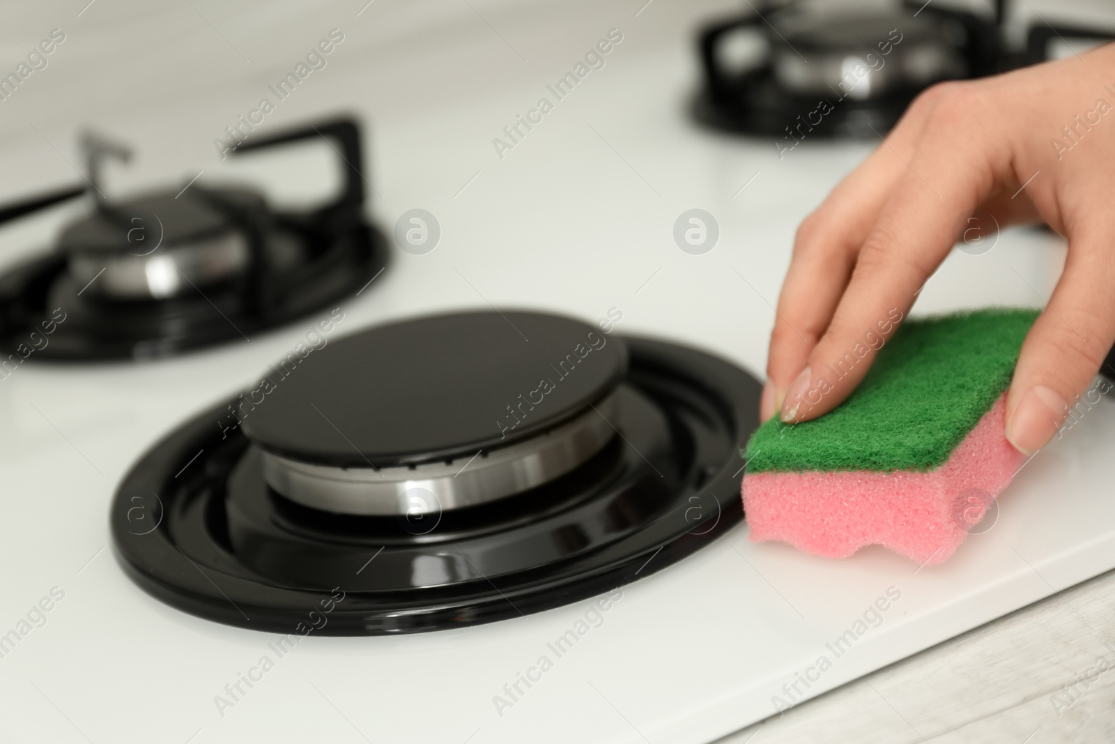 Photo of Woman cleaning gas stove with sponge, closeup