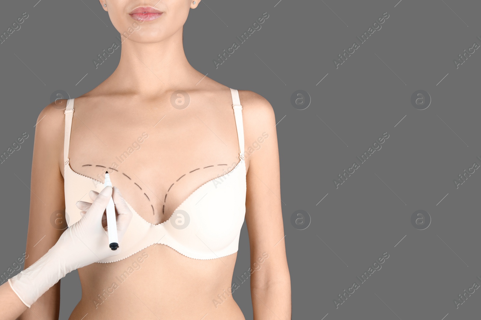 Photo of Doctor drawing marks on patient's breast for cosmetic surgery operation against gray background, closeup. Space for text