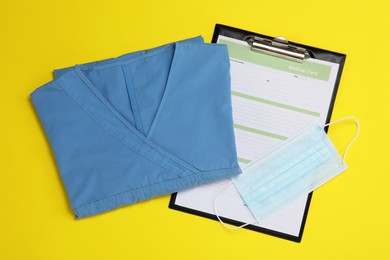 Photo of Medical uniform, face mask and clipboard on yellow background, flat lay