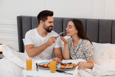 Happy couple having breakfast on bed at home