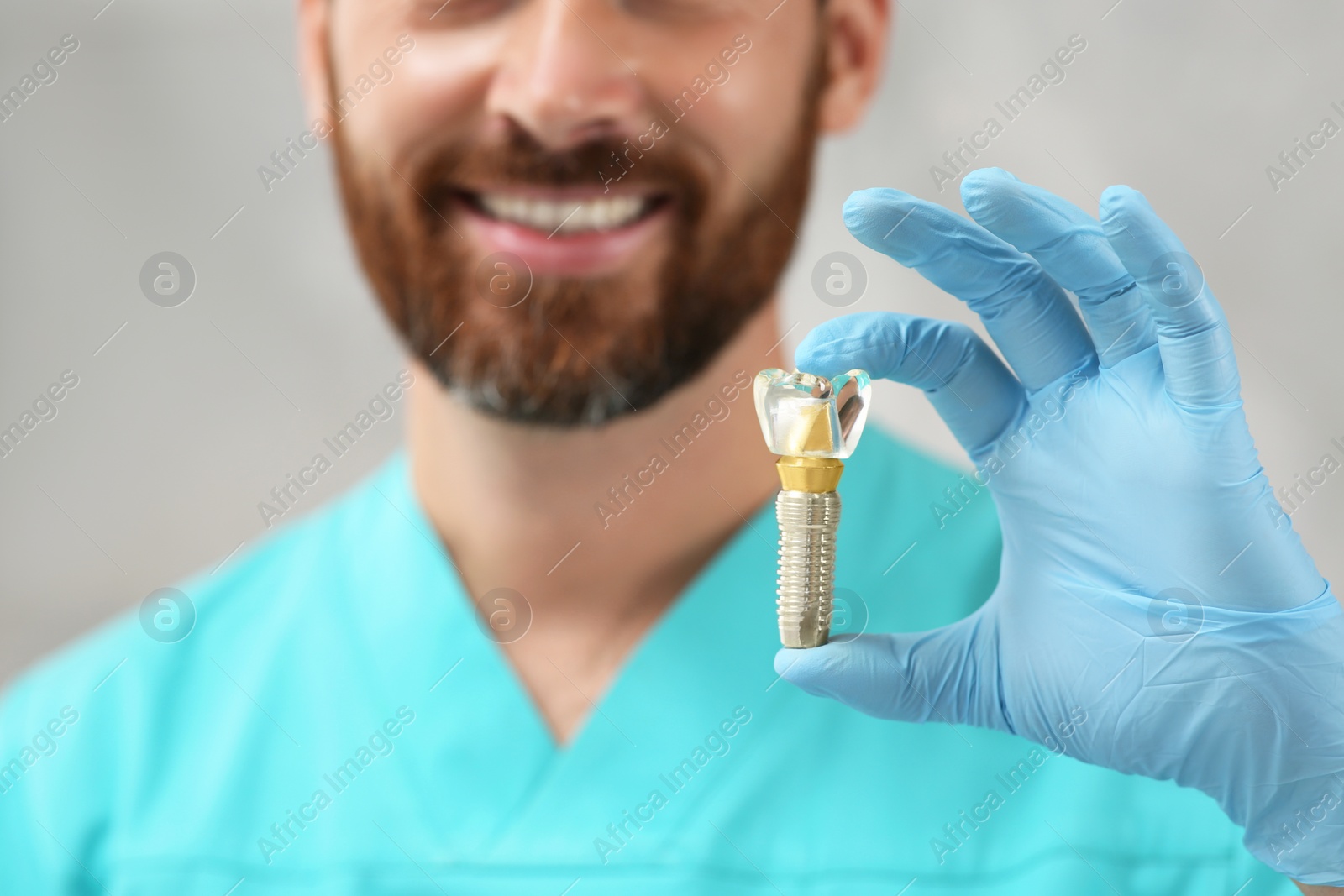 Photo of Dentist holding educational model of dental implant on blurred background, closeup