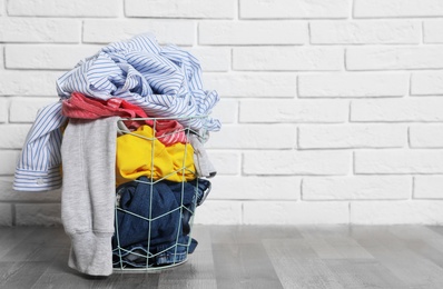 Laundry basket with dirty clothes on floor near brick wall. Space for text