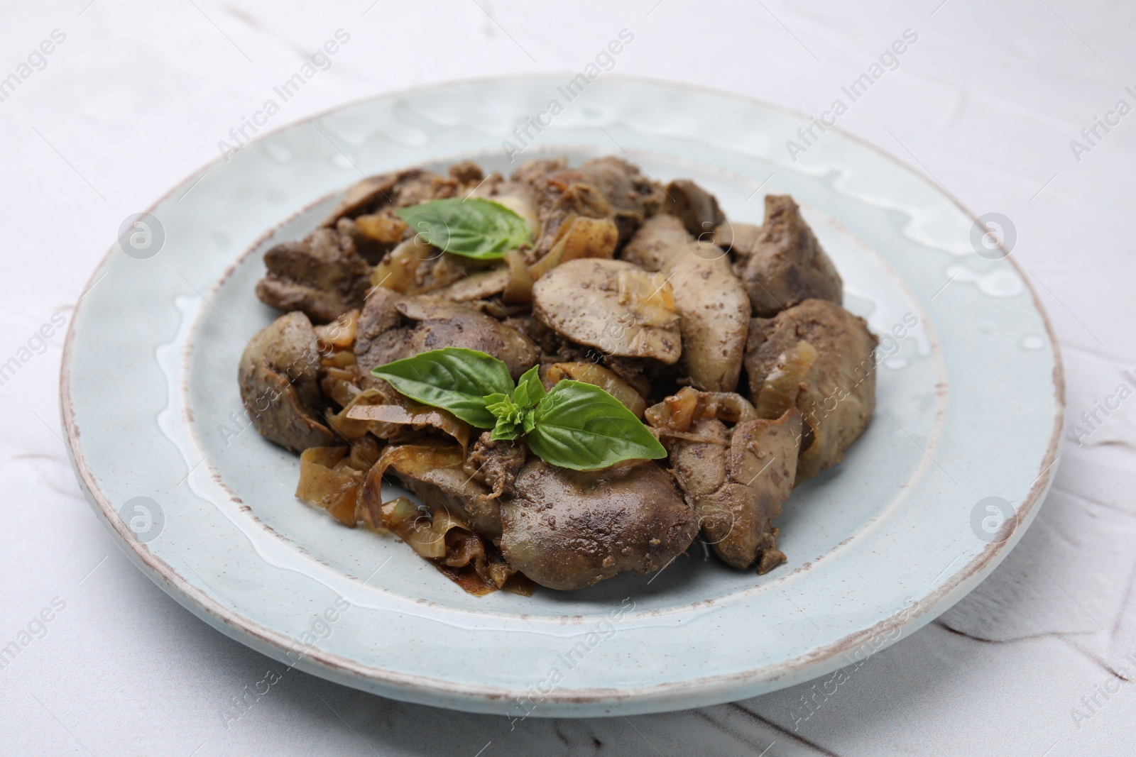 Photo of Plate of delicious fried chicken liver with onion and basil on white textured table, closeup