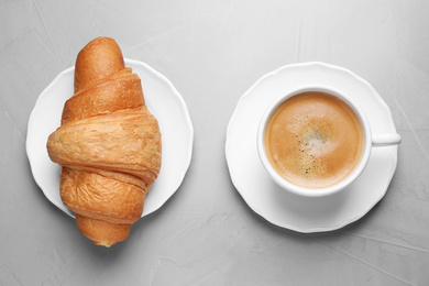 Tasty fresh croissant and coffee on light grey table, flat lay