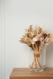 Photo of Beautiful dried flower bouquet in glass vase on wooden table near white wall