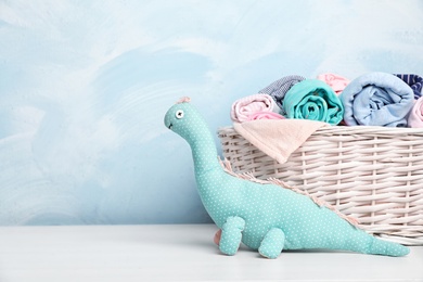 Photo of Basket with baby clothes and toy on table near color wall. Space for text