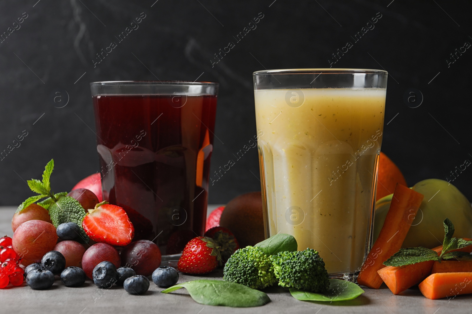 Photo of Delicious juices and fresh ingredients on grey table against black background