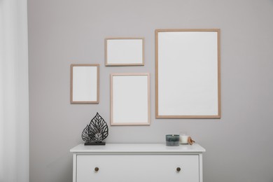 Empty frames hanging on grey wall over white chest of drawers. Mockup for design