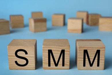 Photo of Wooden cubes with abbreviation SMM (Social media marketing) on light blue background