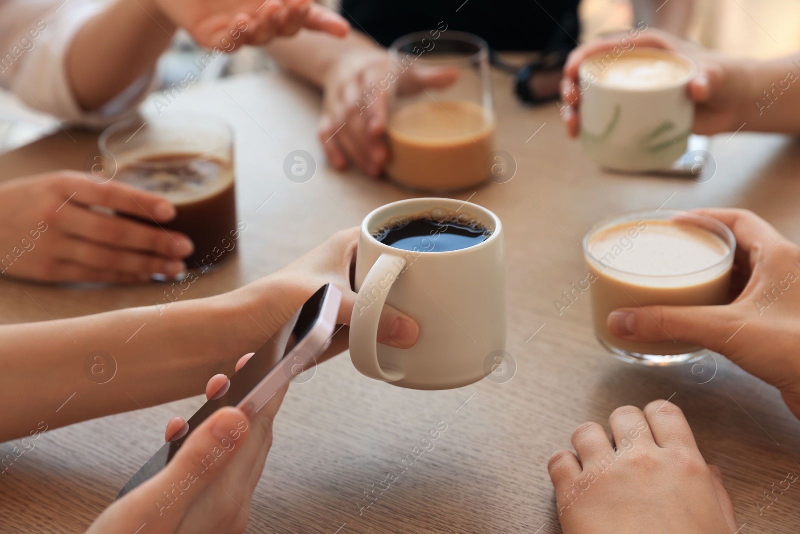 Photo of Friends drinking coffee at wooden table in cafe, closeup