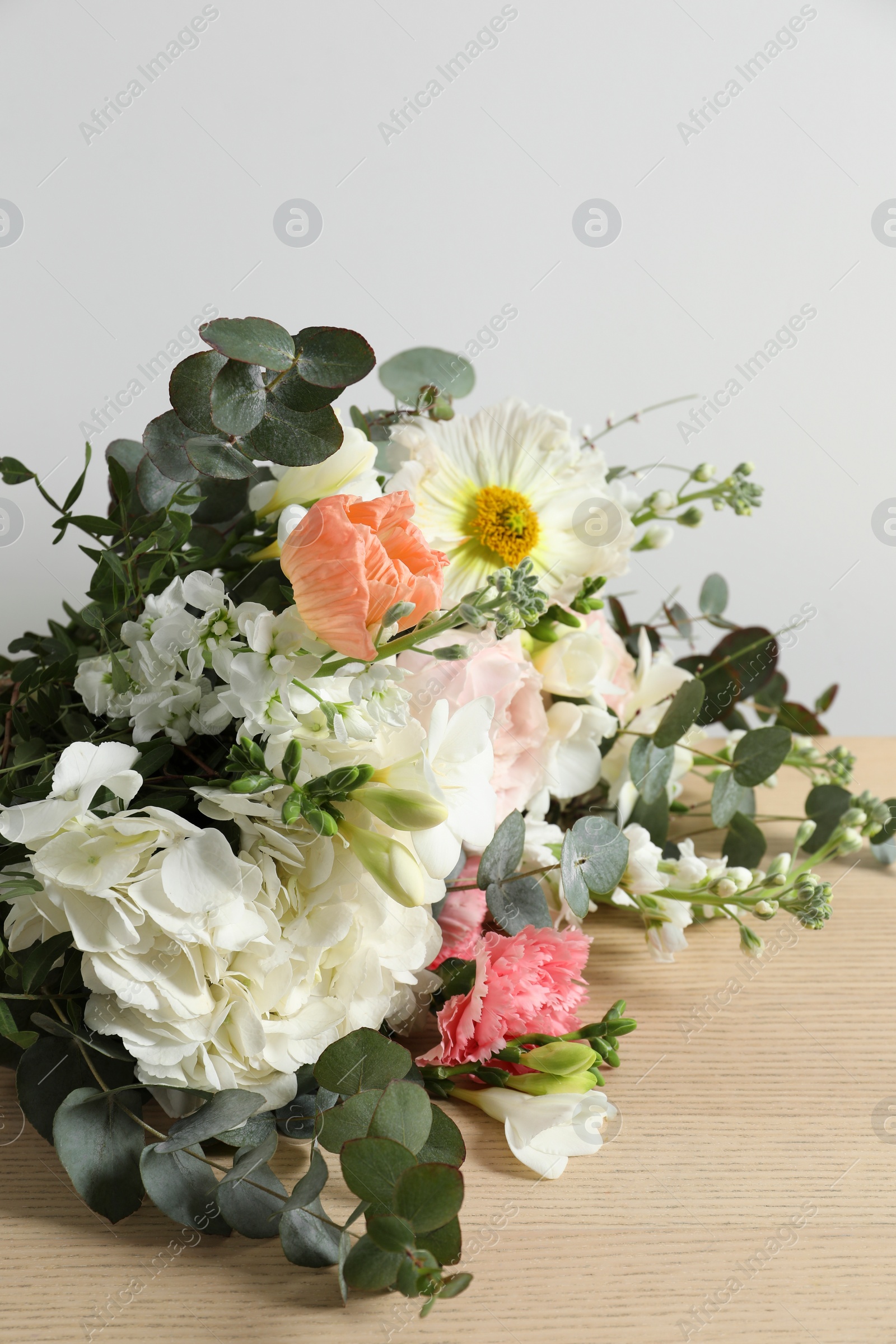 Photo of Bouquet of beautiful flowers on wooden table against white wall, closeup