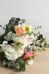 Bouquet of beautiful flowers on wooden table against white wall, closeup