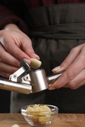 Woman squeezing garlic with press at wooden table, closeup