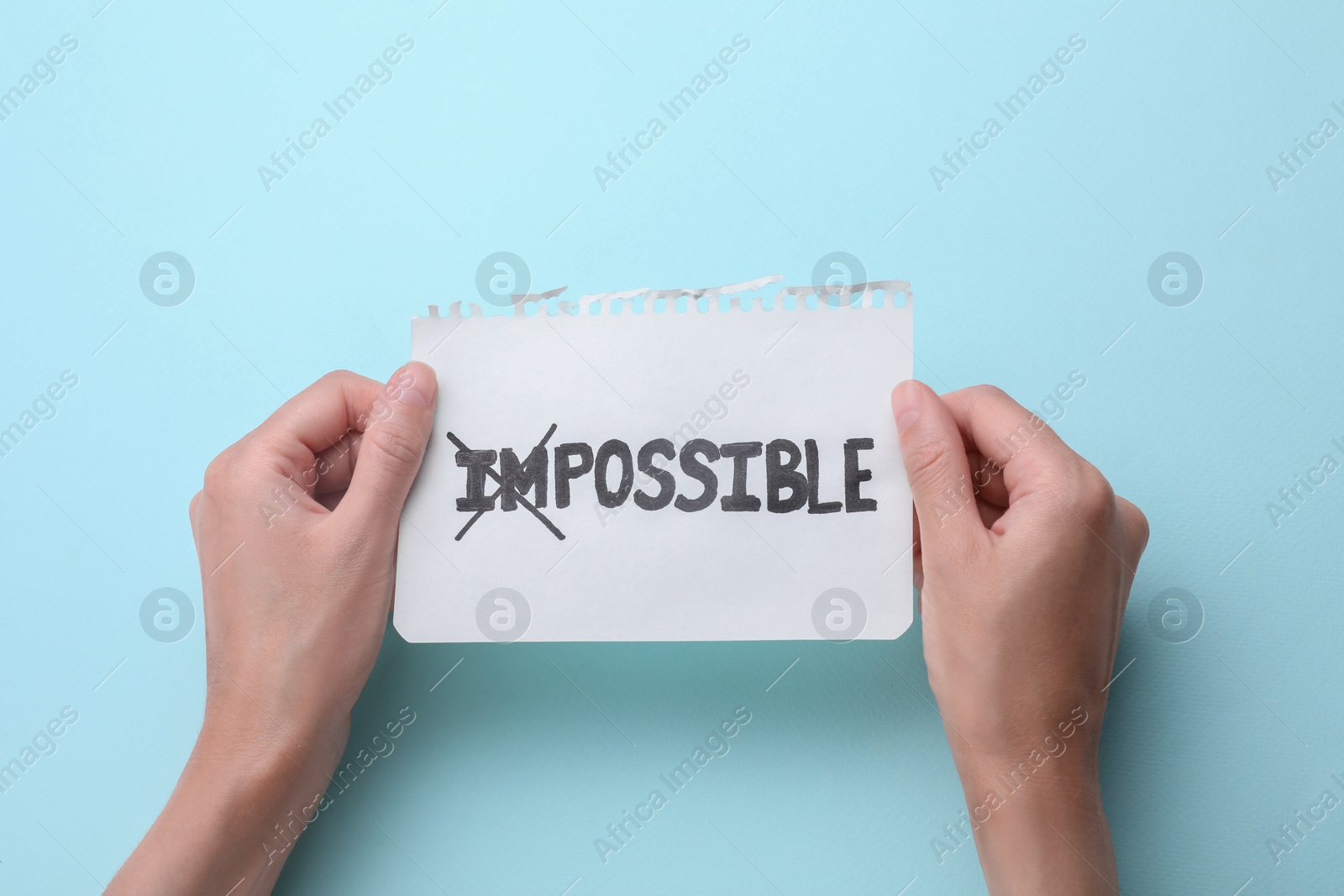 Photo of Motivation concept. Woman holding paper with changed word from Impossible into Possible by crossing over letters I and M on light blue background, top view