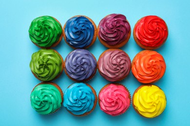 Many delicious colorful cupcakes on light blue background, flat lay