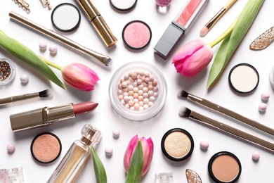 Different makeup products and flowers on white background, top view