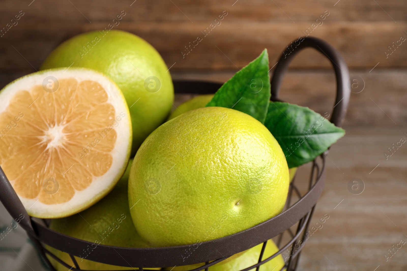 Photo of Whole and cut sweetie fruits in metal basket, closeup