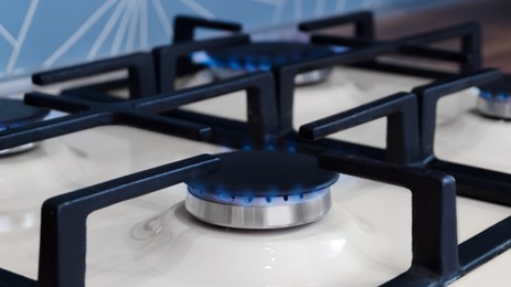 Gas cooktop with burning blue flames in kitchen, closeup. Cooking appliance