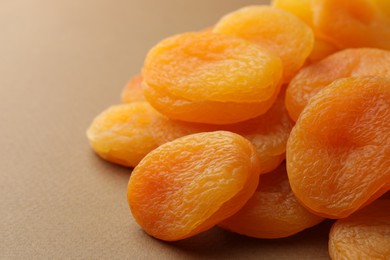 Many tasty dried apricots on pale brown background, closeup