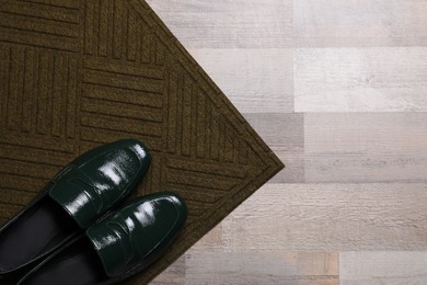 Photo of New clean door mat with shoes on floor, top view. Space for text